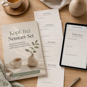 以下が含まれることがあります： カップと花瓶のイラストが描かれたベージュの表紙のKopf-frei Neustart-Setワークブック。Brain Dump、Mental Load、Fokus-Sprint、Wochen-Resetとラベル付けされた複数の印刷済みプランニングシートと、デジタル版を表示するタブレットが並んでいます。