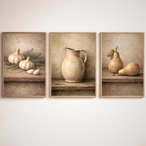 Könnte beinhalten: Set aus drei gerahmten Kunstdrucken mit Stillleben-Kompositionen. Ein Druck zeigt Knoblauchzehen und Zweige auf einem Holzregal. Ein weiterer zeigt einen Keramikkrug. Der dritte Druck zeigt zwei Birnen auf einem Holzregal.