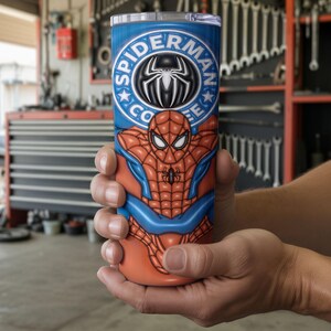 May include: A blue and orange tumbler featuring the Spider-Man character. The tumbler has the words "Spider-Man Coffee" in a circular design at the top. The design includes the Spider-Man logo and a depiction of the character's suit.