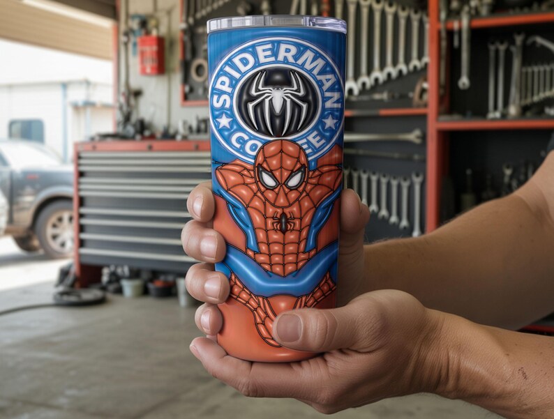 May include: A blue and orange tumbler featuring the Spider-Man character. The tumbler has the words "Spider-Man Coffee" in a circular design at the top. The design includes the Spider-Man logo and a depiction of the character's suit.