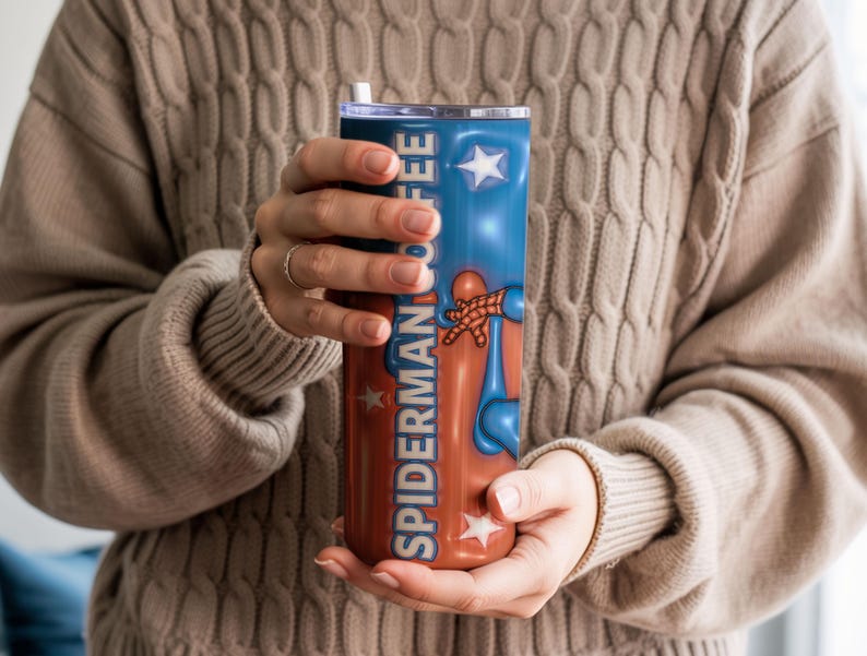 May include: A stainless steel tumbler featuring a design with the words "SPIDERMAN COFFEE" in a vertical layout. The tumbler has a blue and red color scheme with star accents and a graphic of Spider-Man.