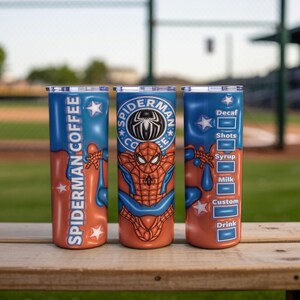 May include: Three stainless steel tumblers with a blue and orange design featuring Spider-Man graphics. One tumbler reads "Spider-Man Coffee", another has the Spider-Man logo, and the third lists coffee options. The tumblers are on a wooden surface.