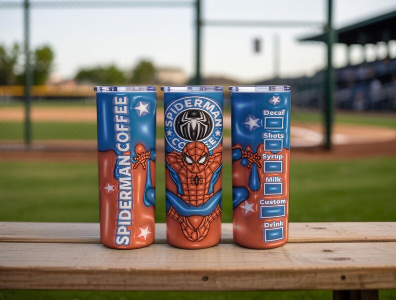 May include: Three stainless steel tumblers with a blue and orange design featuring Spider-Man graphics. One tumbler reads "Spider-Man Coffee", another has the Spider-Man logo, and the third lists coffee options. The tumblers are on a wooden surface.