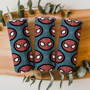 Peut inclure: Trois gobelets en acier inoxydable avec un motif r&eacute;p&eacute;t&eacute; du masque de Spider-Man sur un fond bleu sarcelle avec un motif de toile d'araign&eacute;e. Le masque est rouge avec des yeux blancs et un contour noir.