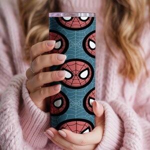 Peut inclure: Un gobelet cylindrique et haut avec un motif r&eacute;p&eacute;t&eacute; du masque de Spider-Man sur un fond bleu sarcelle. Le masque est rouge avec des yeux blancs et un contour noir, sur un motif de toile d'araign&eacute;e.
