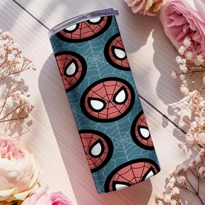 Peut inclure: Un gobelet en acier inoxydable avec un motif r&eacute;p&eacute;t&eacute; du masque de Spider-Man sur un fond bleu sarcelle avec des toiles d'araign&eacute;es blanches. Le gobelet a un couvercle transparent. Entour&eacute; de roses roses et de fleurs blanches.