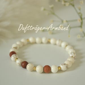 Könnte beinhalten: Ein Armband mit weißen und braunen Perlen, unterbrochen von goldfarbenen Abstandshaltern. Auf dem Armband steht in Schreibschrift "Duftträger-Armband". Die Perlen sind rund und glatt, wodurch ein schlichtes, aber elegantes Design entsteht.
