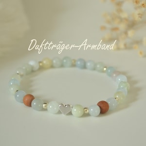 Könnte beinhalten: Ein Armband mit einer Mischung aus hellblauen, grünen und braunen Perlen. Das Armband enthält einen kleinen silbernen Herzanhänger und den Text "Duftträger-Armband". Die Perlen sind mit kleinen goldfarbenen Abstandshaltern aufgereiht.