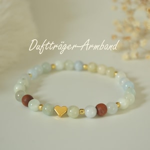 Könnte beinhalten: Ein Perlenarmband mit dem Text "Duftträger-Armband". Das Armband hat eine Mischung aus hellgrünen, weißen und braunen Perlen, durchsetzt mit goldfarbenen Akzenten und einem goldenen Herzanhänger. Die Perlen sind zu einem Kreis aufgefädelt.
