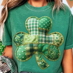 Könnte beinhalten: Grünes T-Shirt mit einem großen Patchwork-Kleeblatt-Design. Das Kleeblatt besteht aus verschiedenen grünen Stoffen, darunter Punkte, Karos und Blumenmuster, die mit goldenem Faden zusammengenäht sind. Ein festliches Oberteil für St. Patrick's Day.