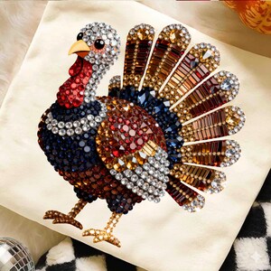 May include: A turkey graphic design composed of multi-colored faceted rhinestones in shades of clear, red, blue, brown, and amber. The turkey features a detailed head, a fan-shaped tail with elongated crystals, and two gold-toned crystal legs.