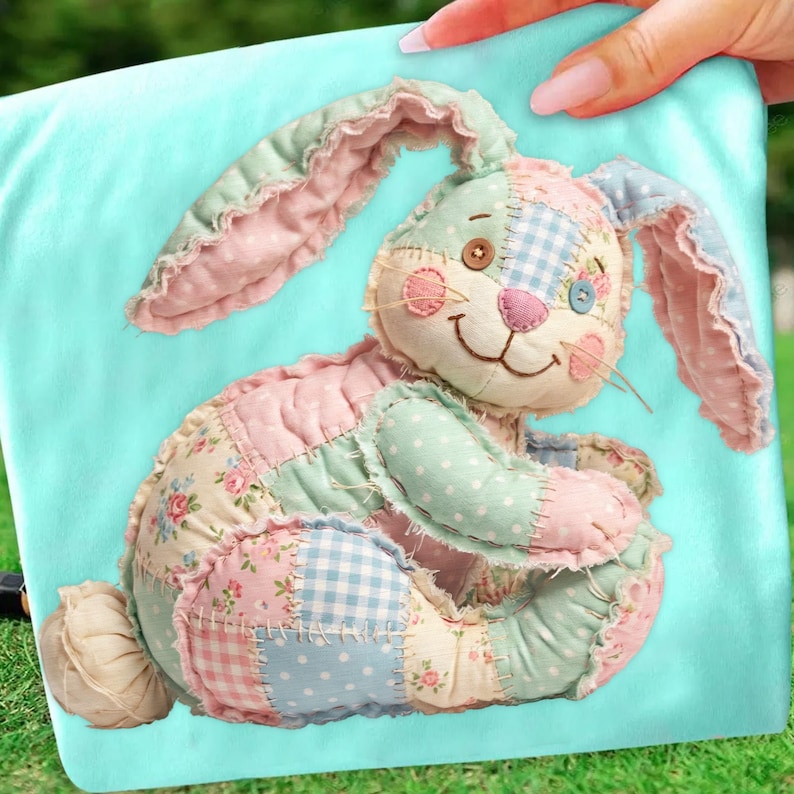 May include: A patchwork bunny rabbit in pastel colors, including pink, blue, and green, is displayed on a light blue background. The bunny features a variety of fabric patterns, including floral, polka dot, and gingham. The bunny has a smiling face and long, floppy ears.