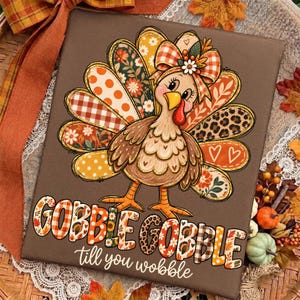 May include: A brown square sign featuring a cartoon turkey with a large bow on its head and a tail made of patterned feathers in orange, white, and brown. The text GOBBLE GOBBLE till you wobble is printed in large, colorful, patterned letters.
