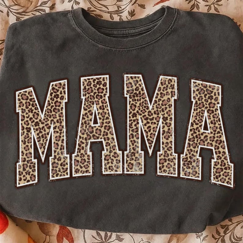 May include: Dark gray sweatshirt with the word "MAMA" in large, bold letters. The letters are filled with a leopard print pattern and outlined in white. The sweatshirt is a casual, comfortable style.