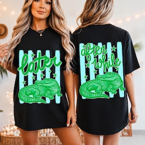 May include: Black t-shirt with a green alligator graphic. The front of the shirt has the word "later" in green script, and the back says "after while". Both sides feature vertical light blue stripes and stars.