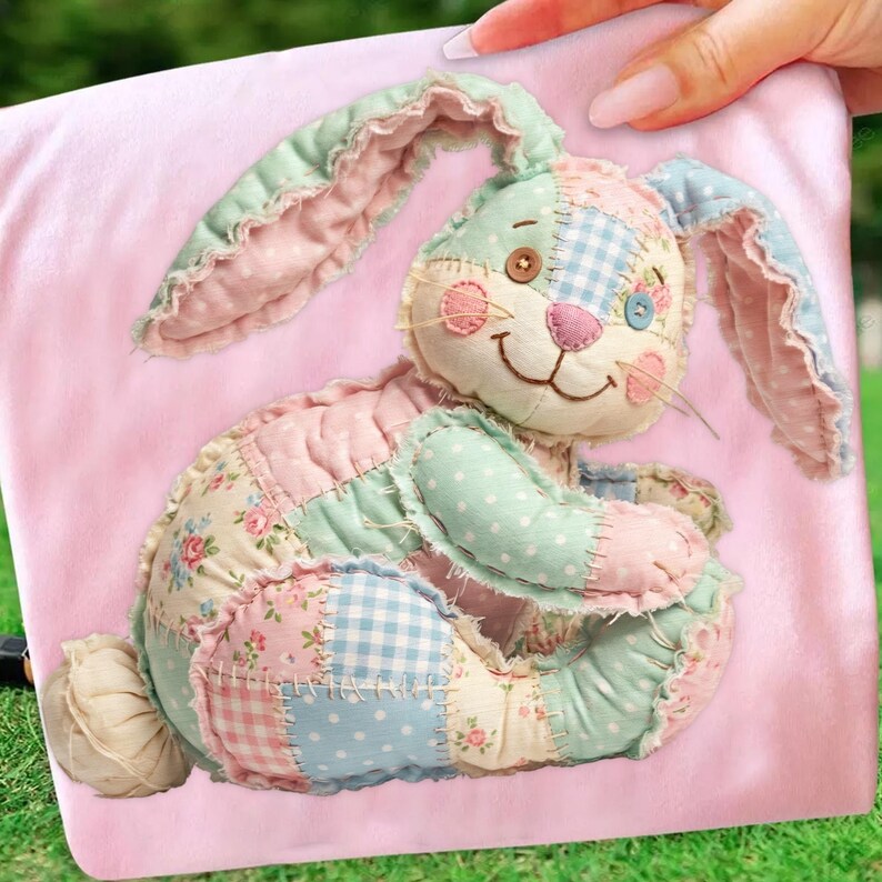 May include: A patchwork bunny rabbit plush toy in pastel colors of pink, blue, and green. The bunny has long ears, a button eye, and a stitched smile. The toy is made of various patterned fabrics, including floral and gingham designs. The bunny is on a pink background.