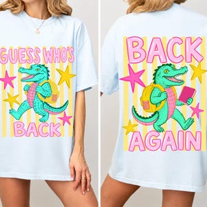 Könnte beinhalten: Ein hellblaues T-Shirt mit einer Grafik eines grünen Alligators, der einen gelben Rucksack trägt. Die Vorderseite zeigt den Text GUESS WHO'S BACK, während die Rückseite den Text BACK AGAIN zeigt. Das Design enthält gelbe Streifen und rosa Sterne.