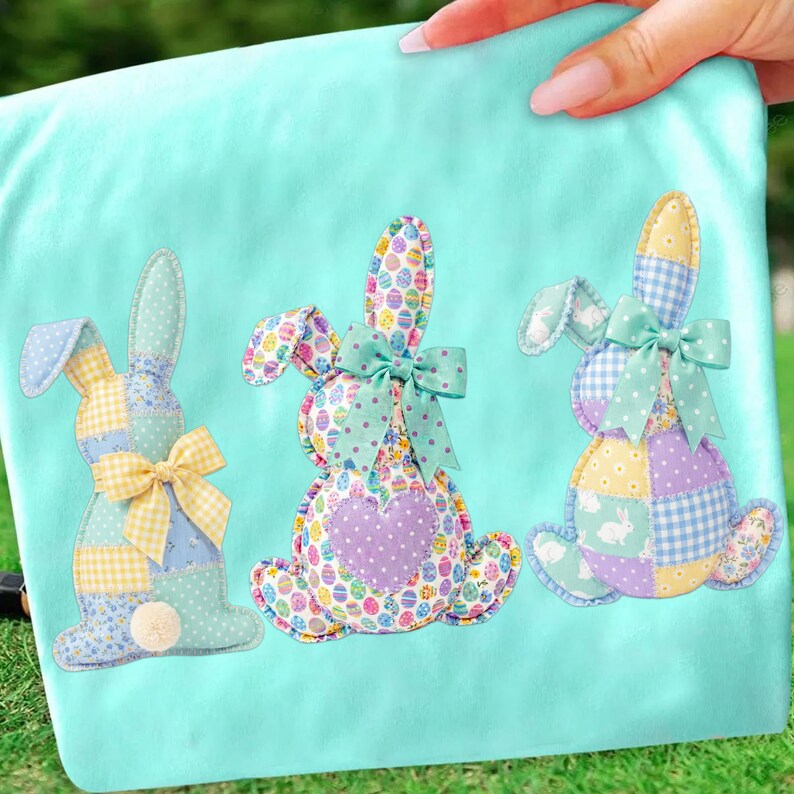 May include: A light blue fabric with three appliqued Easter bunny designs. Each bunny is made of patchwork fabric with pastel colors, polka dots, and egg patterns. The bunnies have bows and a fluffy tail.