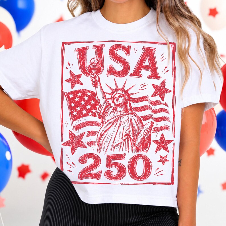 May include: White t-shirt with a red graphic featuring the Statue of Liberty, the American flag, stars, and the text "USA 250". The design is a patriotic celebration of the United States.