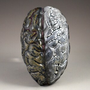 May include: A ceramic sculpture of a human brain, painted in silver and gold with a red line down the middle.
