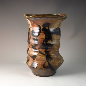 May include: A brown and black ceramic vase with a textured surface and abstract design.
