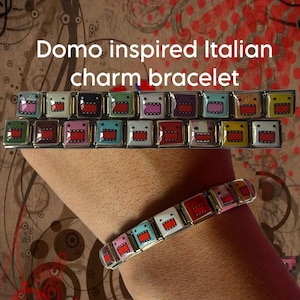 Op de afbeelding: Een Italiaanse bedelarmband met meerdere vierkante schakels, elk met een kleurrijk Domo-figuurtje met een brede mond en scherpe tanden. De tekst "Domo inspired Italian charm bracelet" staat boven de schakels van de armband.