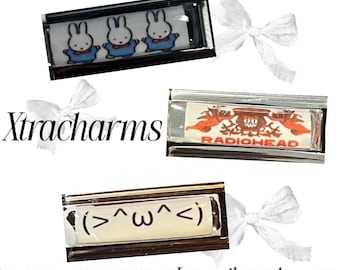 May include: Three rectangular silver-toned metal charms. The top charm features three white rabbits in blue shirts. The middle charm displays an orange graphic with the text RADIOHEAD. The bottom charm shows a brown emoticon reading (>^ω^<).