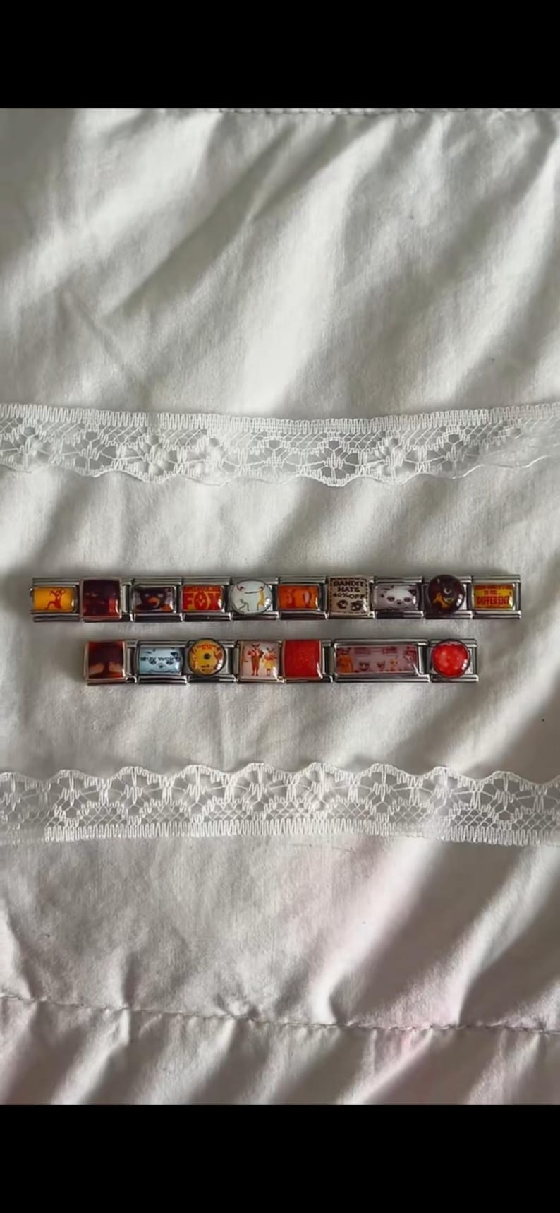 Op de afbeelding: Twee zilverkleurige modulaire schakelarmbanden met een reeks rechthoekige en ronde bedels met diverse kleurrijke grafische prints, waaronder tekst, dierillustraties en abstracte patronen, gerangschikt in een horizontale rij op een witte ondergrond.