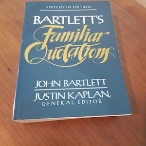 Könnte beinhalten: Ein gebundenes Buch mit dem Titel "Bartlett's Familiar Quotations, Sixteenth Edition" wird gezeigt. Das Buch hat einen dunkelblauen Einband mit goldener Schrift. Die Namen der Autoren, John Bartlett und Justin Kaplan, sind ebenfalls sichtbar.