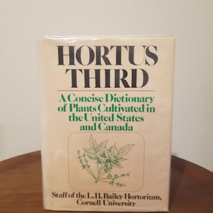 Peut inclure: Livre intitulé "HORTUS THIRD" avec le sous-titre "A Concise Dictionary of Plants Cultivated in the United States and Canada". La couverture est blanc cassé avec du texte noir et une illustration botanique verte.