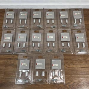 May include: Several clear plastic packs of hardware components. Each pack contains a small grey box with the word "RULL" printed on it, plus silver cylindrical pieces and screws. The packs are arranged on a wooden surface.
