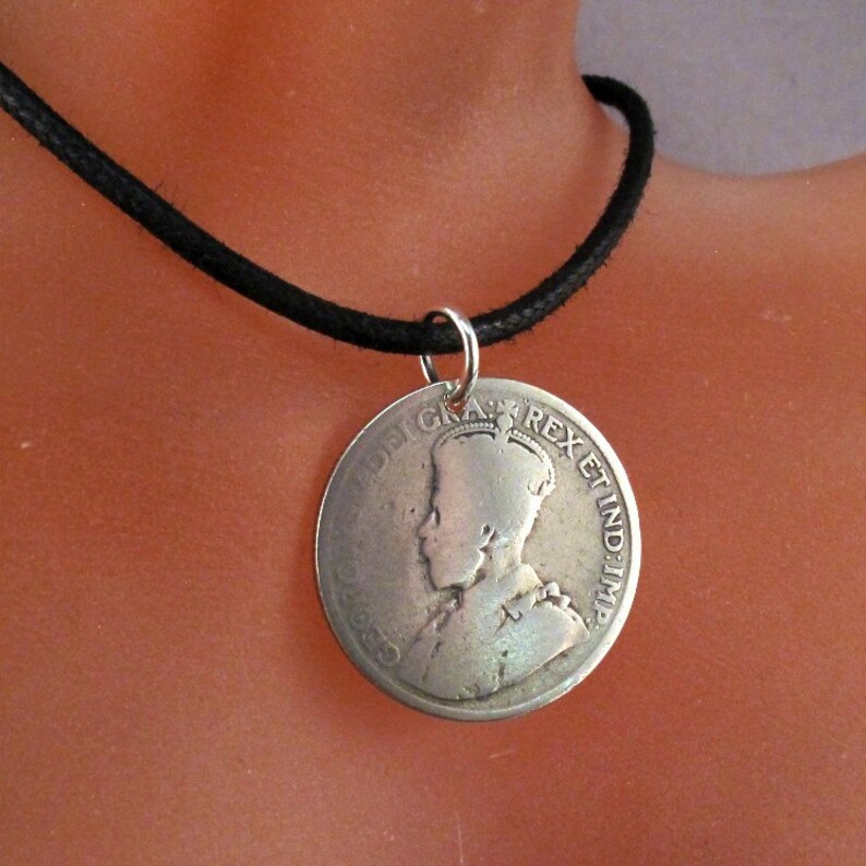May include: A silver coin pendant necklace with a profile of a woman wearing a crown. The coin has the inscription "GEORGIUS REX ET IND: IMP:" around the edge. The necklace is made with a black cord.