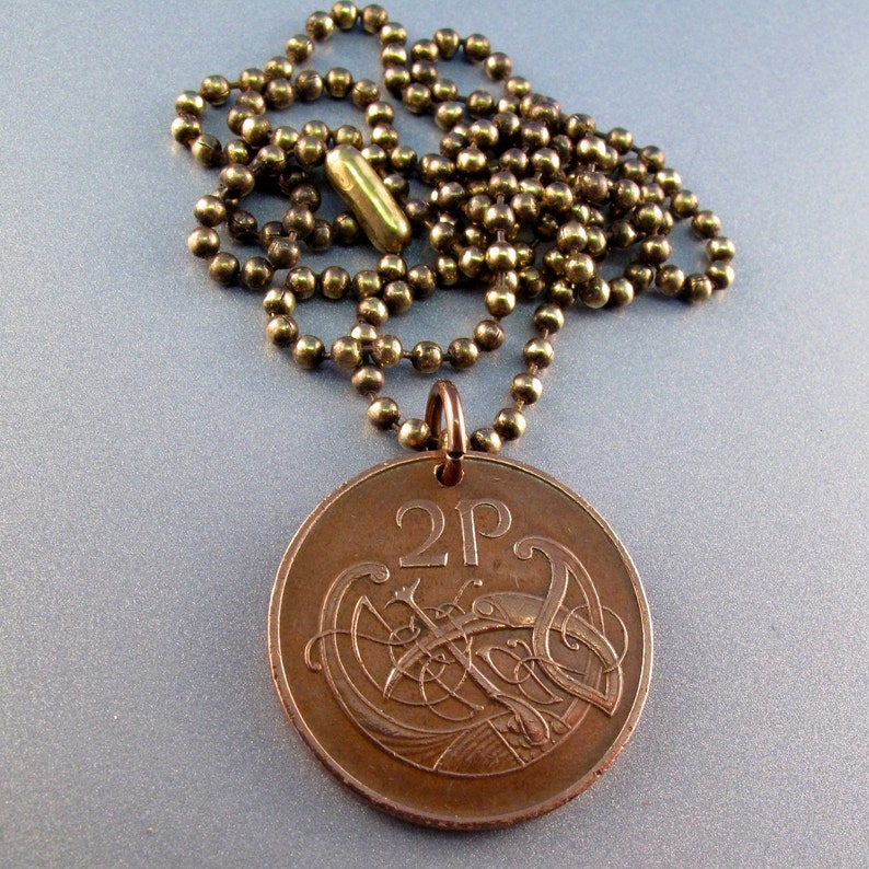 May include: A gold chain necklace with a 2 pence coin pendant. The coin features a Celtic knot design.