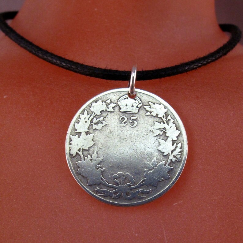 May include: A silver coin pendant necklace with a black cord. The coin features a wreath of maple leaves and the number "25" with a crown above it.