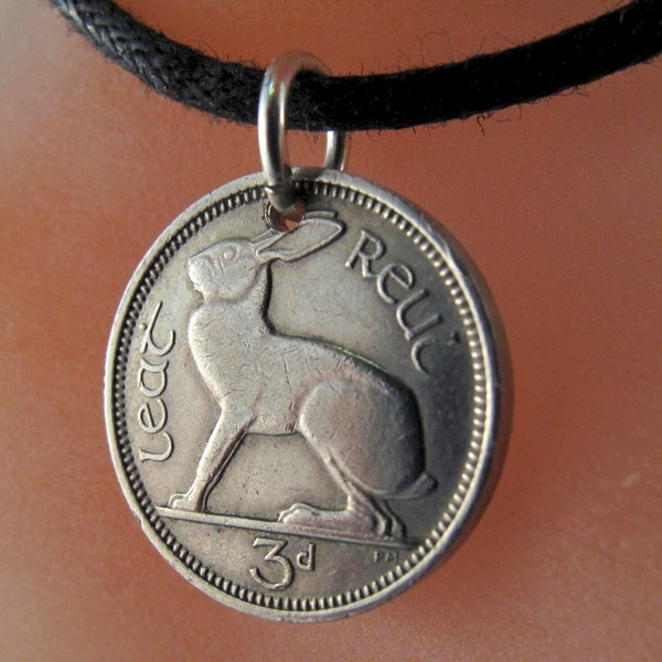 Op de afbeelding: Een zilveren Ierse 3 pence munt met een haas erop, aan een zwarte koordsnoer. De munt heeft de woorden "Eire" en "3d" erop.
