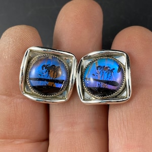 May include: A pair of silver cufflinks with square frames and round blue and purple butterfly wing inlays.