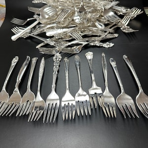 May include: A set of 16 silver forks with ornate handles. The forks are arranged in two rows of eight, with the tines facing up. The forks are all the same size and style.