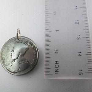 May include: Silver coin pendant with a profile of a woman wearing a crown and the text "GEORGIVS V DEI GRA REX ET IND IMP" around the edge. The coin is about 1 1/2 inches in diameter.