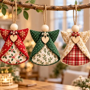May include: Three fabric angel ornaments hanging from a branch. Each features a wooden bead head, a small wooden heart, and a jute string loop. The first is red with gold snowflakes and holly, the second green with white dots and sprigs, and the third cream with gold foliage and a red plaid base.