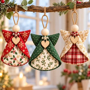 Puede incluir: Tres adornos de ángeles de tela colgados de una rama. Cada uno cuenta con una cabeza de cuenta de madera, un pequeño corazón de madera y alas y faldas de tela estampada. Los diseños incluyen rojo con copos de nieve, verde con puntos.