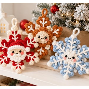 May include: Three crocheted snowflake ornaments featuring smiling faces with rosy cheeks. One is red and white with a Santa Claus design, one is brown and white with a gingerbread theme, and one is light blue and white with a winter snowflake design.