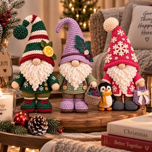 May include: Three crocheted gnome figurines with long white beards and tall pointed hats. The first gnome wears a green striped hat with a lemon slice, the second a lavender hat with leaves, and the third a red hat with white snowflakes.