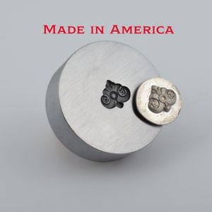 May include: A metal stamp with a floral design. The stamp is made in America. The stamp is shown next to a metal block with the same design.