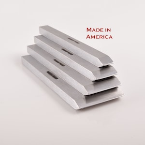 May include: Four silver metal chisels stacked on top of each other. The chisels are beveled on one end and have a flat surface on the other. The chisels are made in America.
