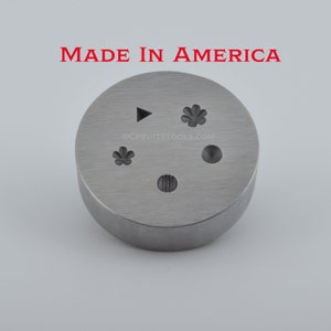 May include: A silver metal disc with five different designs engraved into it. The designs include a triangle, a flower, a circle, a flower, and a line pattern. The disc is labeled "MADE IN AMERICA" and "@CPRUITTTOOLS.COM".