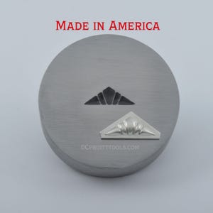 May include: A circular, brushed metal object with two triangular designs. The top design is black, and the bottom is silver. The text "MADE IN AMERICA" is in red at the top. The website address "CPRUITTOOLS.COM" is at the bottom.