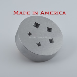 May include: A silver metal tool with five pyramid-shaped indentations. The tool is round and has a smooth surface. The text "MADE IN AMERICA" is printed above the tool. The text "OCPRUITTTOOLS.COM" is printed below the tool.