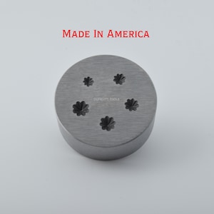 May include: A circular metal tool with five flower-shaped cutouts. The tool is made of brushed metal and has the words "MADE IN AMERICA" printed in red at the top. The brand name "CCFRUIT TOOLS" is printed at the bottom.