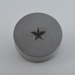 May include: A round, silver-colored metal stamp with a five-pointed star design in the center.