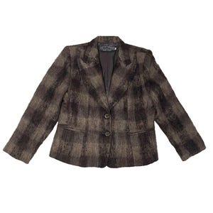 May include: A brown and dark gray plaid blazer with a textured, fuzzy finish. The jacket features a notched lapel, long sleeves, two front buttons for closure, and two horizontal welt pockets. A dark interior lining is visible at the collar.